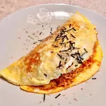 Spicy Korean Buldak Omelet with melted cheese and sausage on a black plate, garnished with green onions.