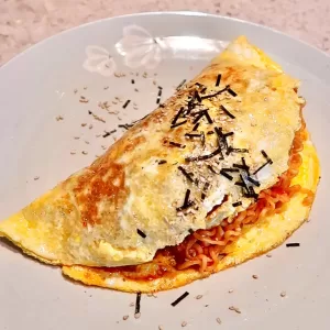 Spicy Korean Buldak Omelet with melted cheese and sausage on a black plate, garnished with green onions.