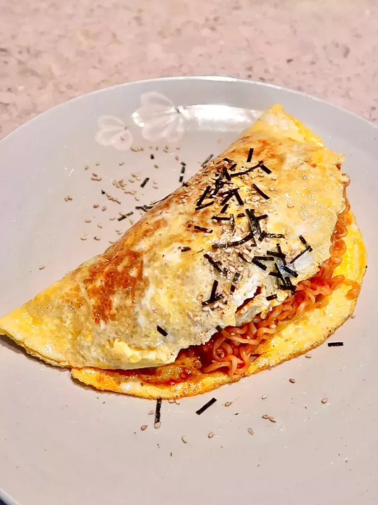 Spicy Korean Buldak Omelet with melted cheese and sausage on a black plate, garnished with green onions.